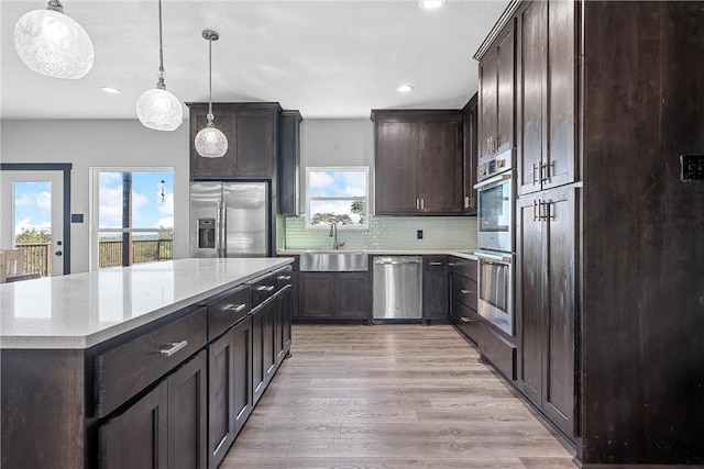 kitchen with light wood-type flooring, stainless steel appliances, sink, decorative light fixtures, and a center island