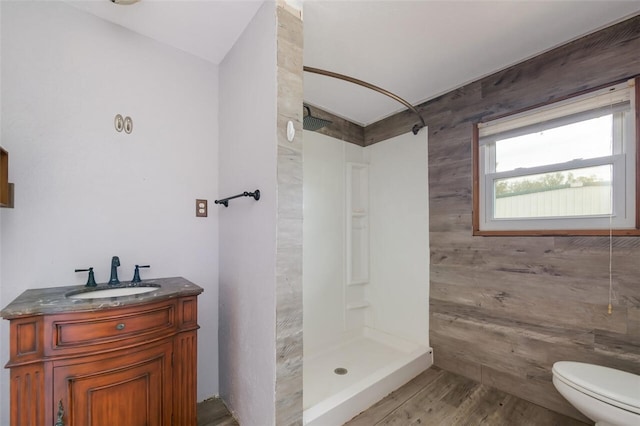 bathroom featuring walk in shower, vanity, wooden walls, wood-type flooring, and toilet