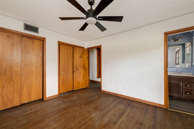 unfurnished bedroom featuring ensuite bath, a textured ceiling, ceiling fan, dark hardwood / wood-style floors, and multiple closets