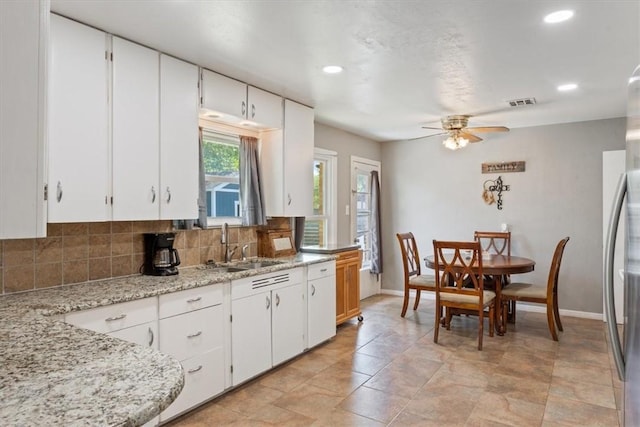 kitchen with decorative backsplash, ceiling fan, light stone countertops, and white cabinetry