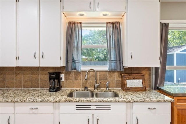 kitchen with tasteful backsplash, light stone countertops, sink, and white cabinets