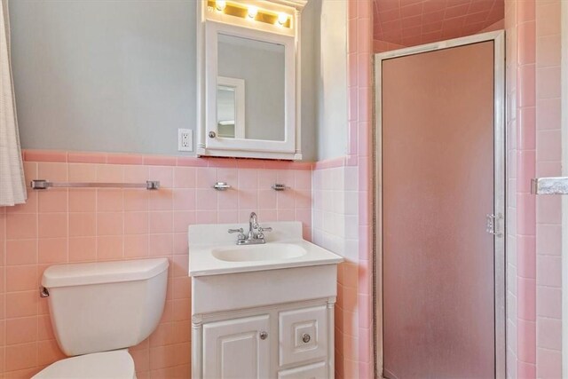 bathroom with vanity, toilet, a shower with door, and tile walls