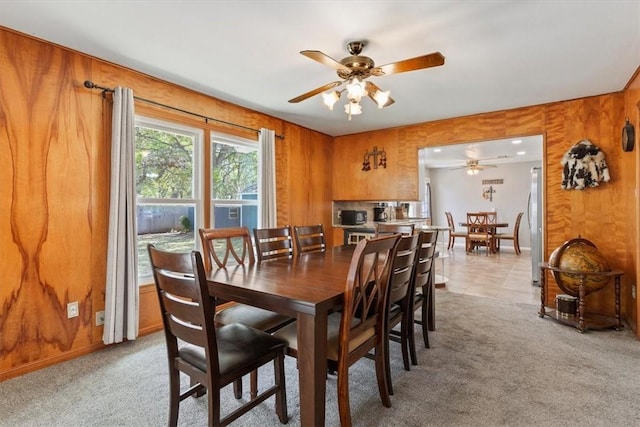 carpeted dining space with ceiling fan and wood walls