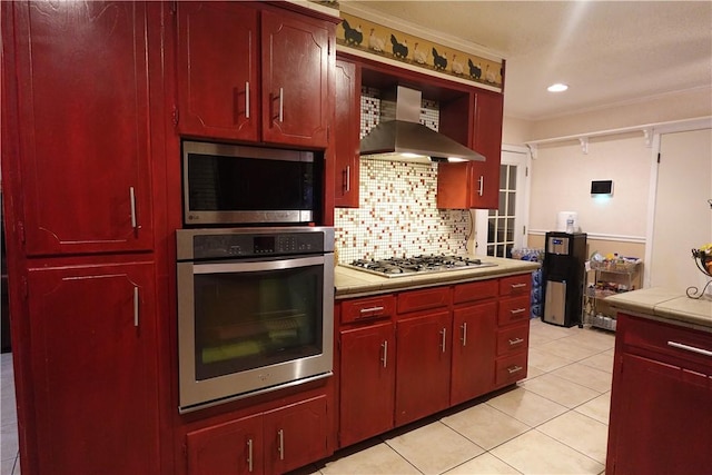 kitchen featuring crown molding, wall chimney exhaust hood, decorative backsplash, light tile patterned floors, and stainless steel appliances