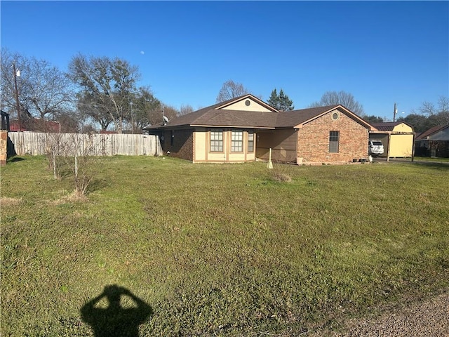 rear view of house with a lawn, brick siding, and fence