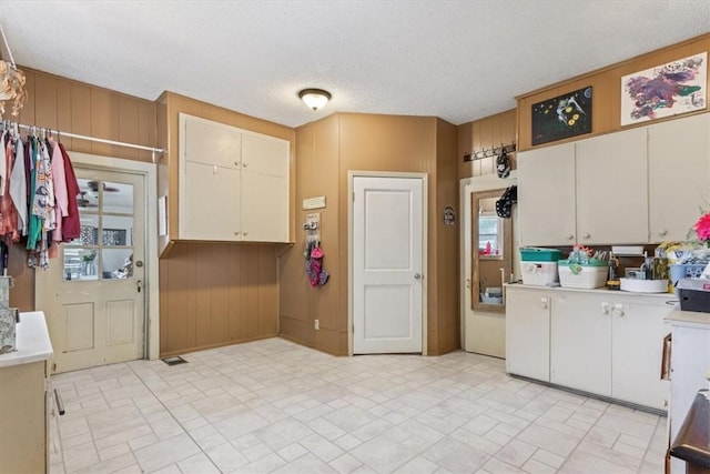 kitchen with white cabinets, a textured ceiling, and wooden walls