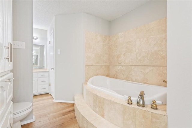 bathroom with vanity, a textured ceiling, wood-type flooring, a relaxing tiled tub, and toilet