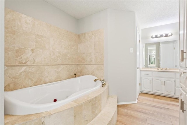 bathroom featuring vanity, hardwood / wood-style floors, a textured ceiling, and tiled tub