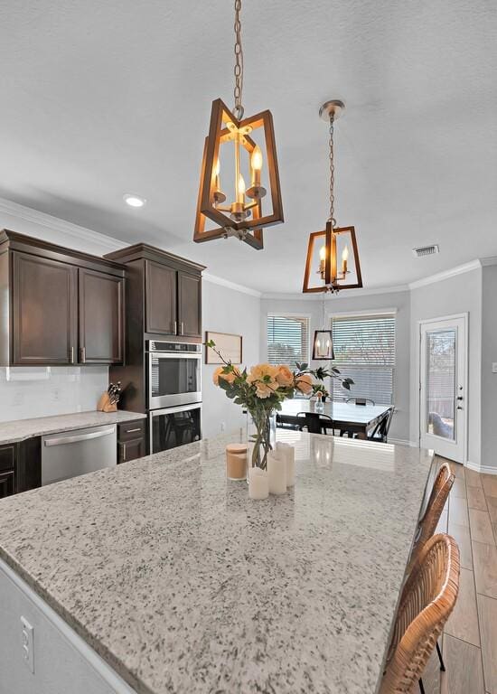 kitchen with dark brown cabinetry, visible vents, appliances with stainless steel finishes, light stone countertops, and crown molding