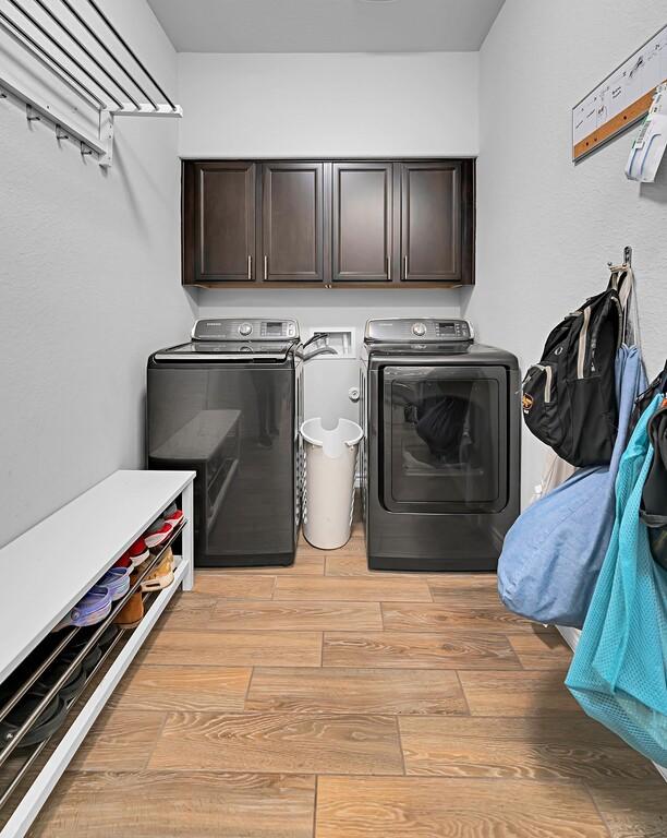 clothes washing area with light wood finished floors, independent washer and dryer, and cabinet space