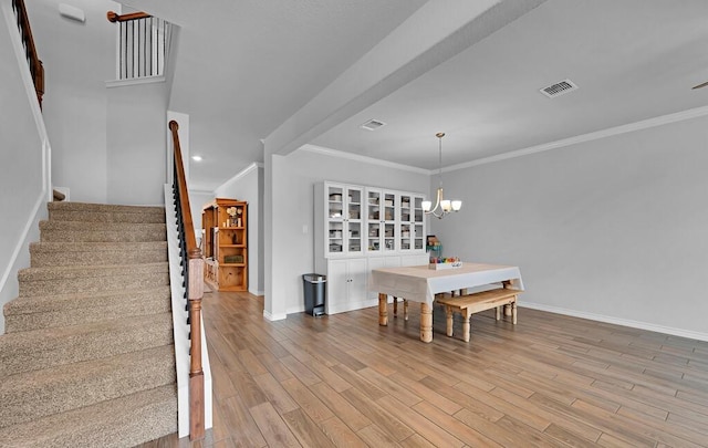 dining space with a notable chandelier, wood finished floors, visible vents, baseboards, and stairs