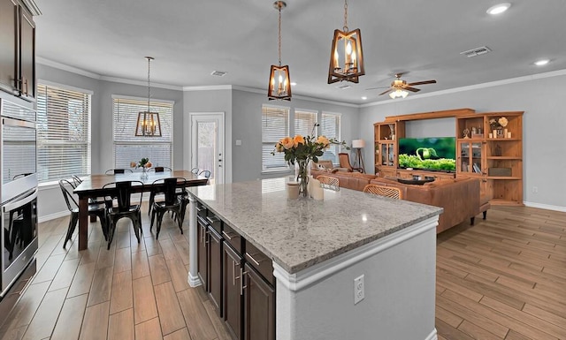 kitchen featuring decorative light fixtures, visible vents, light wood-style flooring, ornamental molding, and light stone countertops