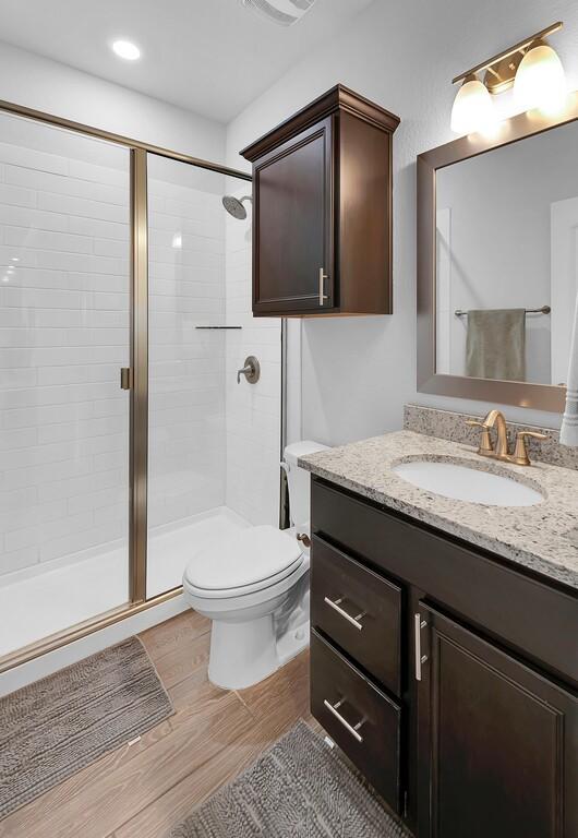 bathroom featuring vanity, wood finished floors, a shower stall, and toilet