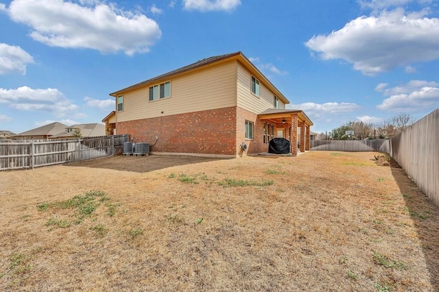 rear view of house featuring cooling unit, brick siding, a yard, and a fenced backyard