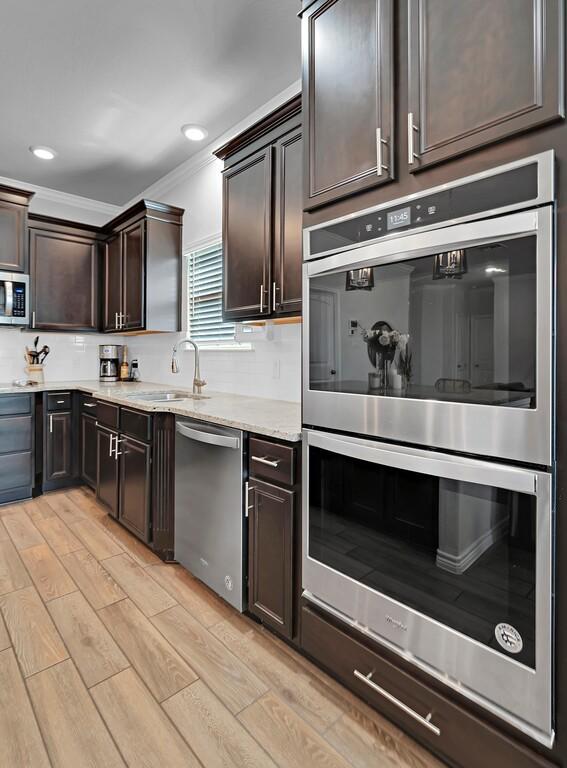 kitchen featuring dark brown cabinetry, light wood finished floors, ornamental molding, stainless steel appliances, and a sink