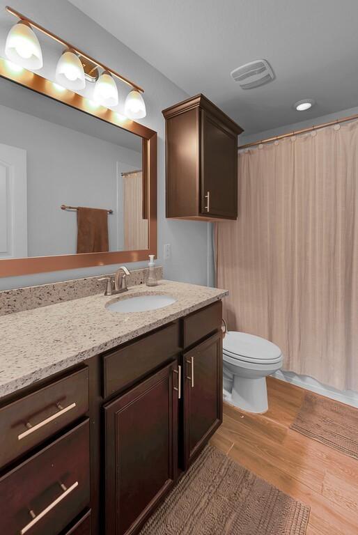 bathroom with visible vents, a shower with shower curtain, toilet, wood finished floors, and vanity