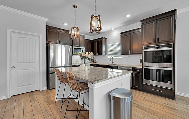 kitchen with stainless steel appliances, a sink, dark brown cabinets, light wood finished floors, and a kitchen bar