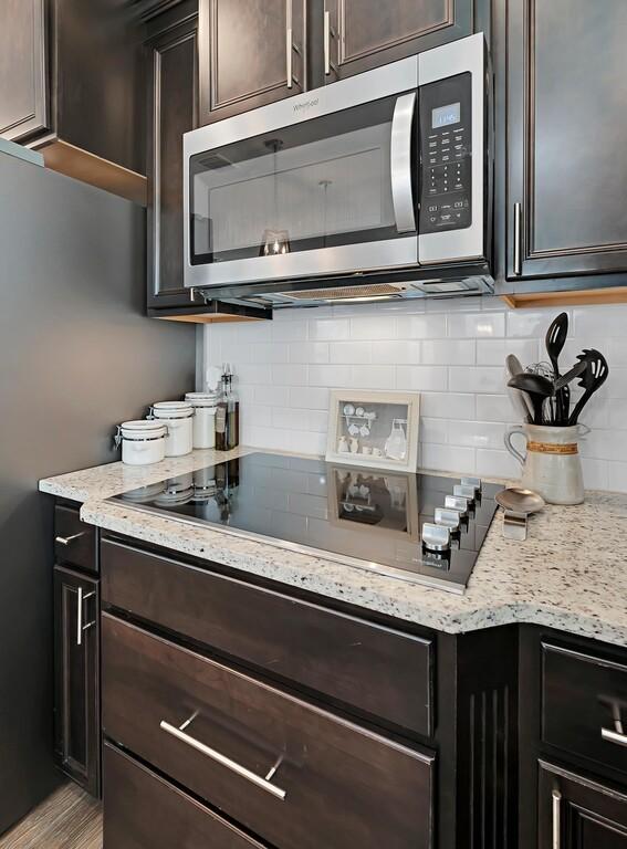 kitchen with light stone countertops, stainless steel microwave, black electric cooktop, and decorative backsplash