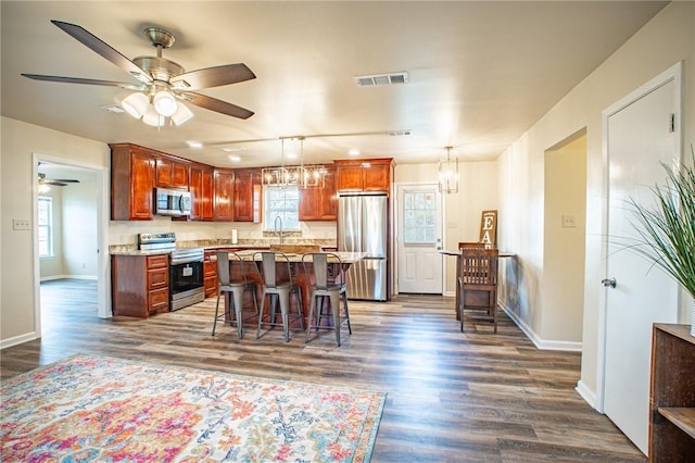 kitchen featuring a breakfast bar area, appliances with stainless steel finishes, dark hardwood / wood-style flooring, pendant lighting, and ceiling fan