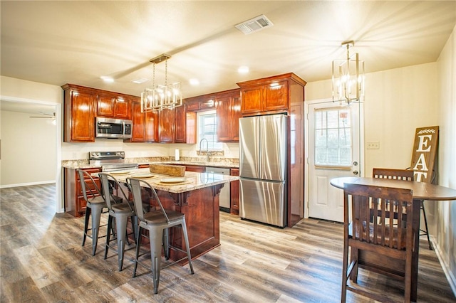 kitchen with a kitchen island, appliances with stainless steel finishes, hardwood / wood-style floors, a kitchen breakfast bar, and hanging light fixtures