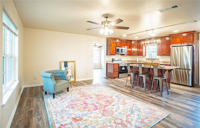 kitchen featuring stainless steel appliances, wood-type flooring, hanging light fixtures, and a breakfast bar area