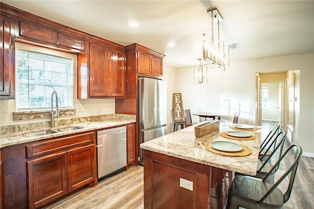 kitchen with appliances with stainless steel finishes, sink, pendant lighting, and light hardwood / wood-style flooring