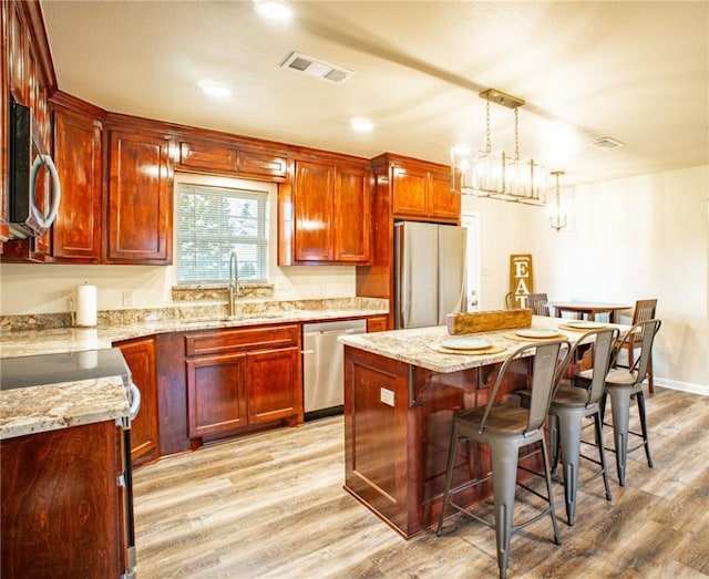 kitchen with light stone counters, sink, decorative light fixtures, and stainless steel appliances