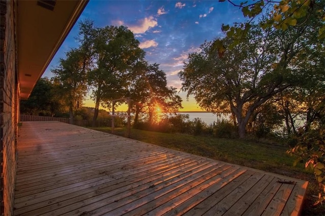 deck at dusk with a yard and a water view