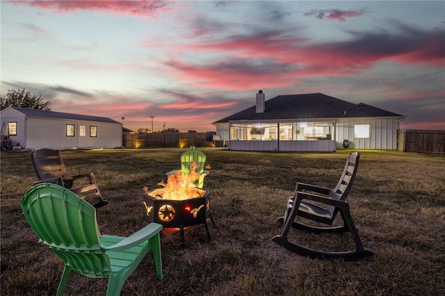 back house at dusk featuring an outdoor fire pit and a lawn