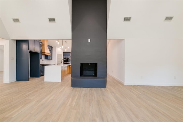 kitchen featuring a fireplace, a towering ceiling, decorative light fixtures, and light wood-type flooring