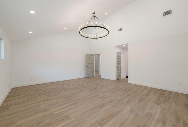 unfurnished room with a chandelier, high vaulted ceiling, and light hardwood / wood-style floors