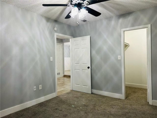 unfurnished bedroom featuring a textured ceiling, a closet, a spacious closet, and ceiling fan