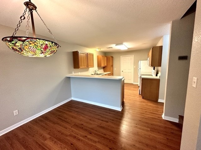 kitchen featuring dark wood-type flooring, sink, hanging light fixtures, a textured ceiling, and kitchen peninsula