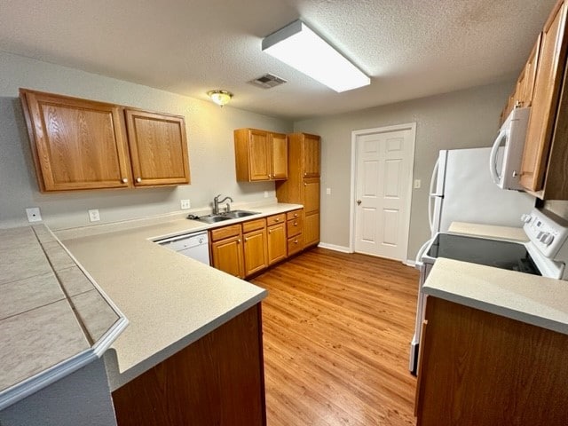 kitchen with sink, kitchen peninsula, light hardwood / wood-style floors, a textured ceiling, and white appliances