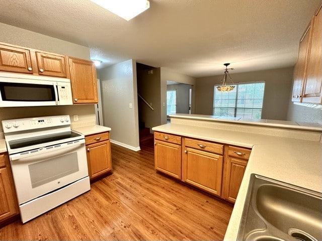 kitchen featuring kitchen peninsula, white appliances, sink, pendant lighting, and light hardwood / wood-style floors