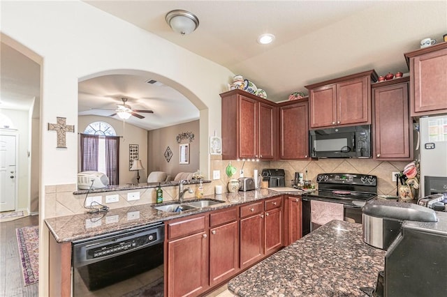 kitchen featuring sink, hardwood / wood-style flooring, black appliances, vaulted ceiling, and dark stone counters