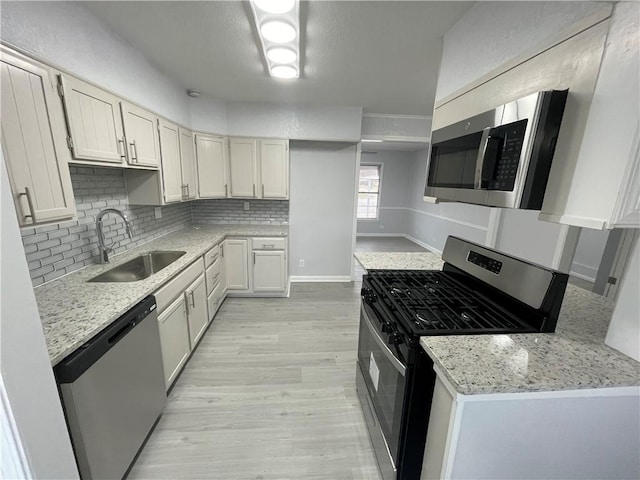 kitchen featuring appliances with stainless steel finishes, white cabinetry, sink, backsplash, and light stone counters