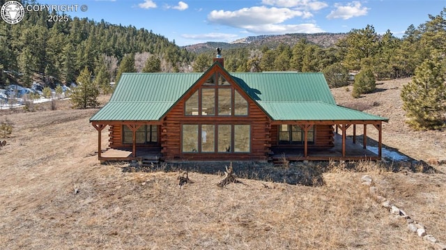 back of house featuring a porch, log exterior, a mountain view, and metal roof