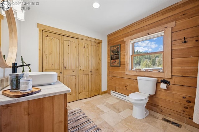 bathroom featuring a baseboard heating unit, toilet, baseboards, visible vents, and wood walls