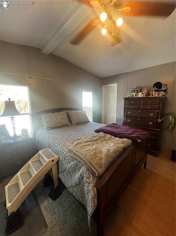 bedroom with vaulted ceiling with beams, hardwood / wood-style flooring, a textured ceiling, and ceiling fan