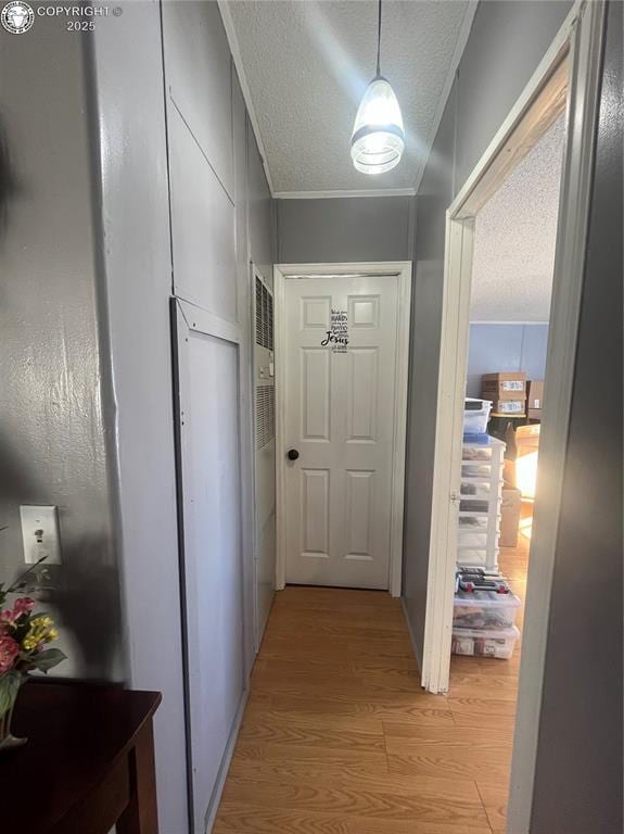 corridor featuring crown molding, a textured ceiling, and light wood-type flooring