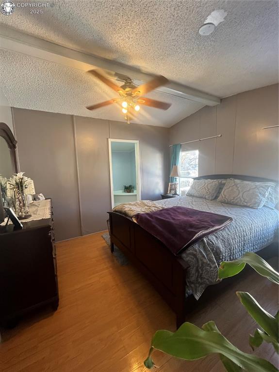 bedroom with hardwood / wood-style flooring, ceiling fan, lofted ceiling with beams, and a textured ceiling