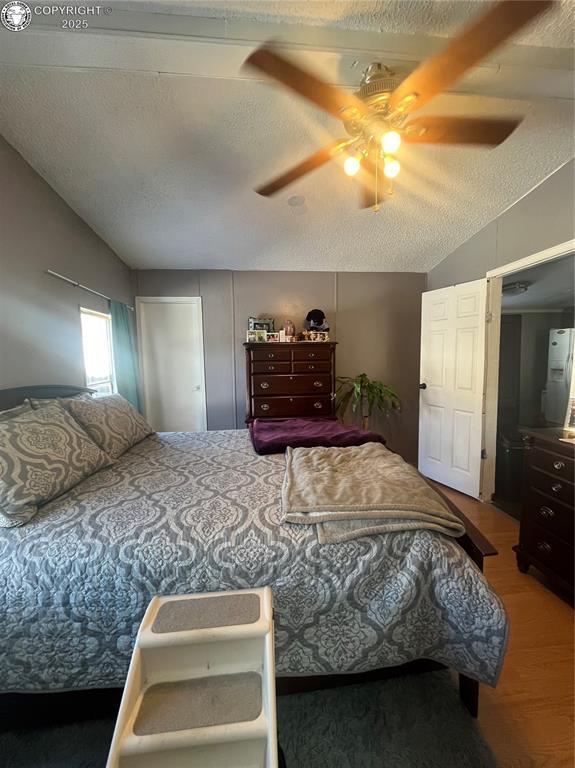 bedroom featuring lofted ceiling, hardwood / wood-style floors, a textured ceiling, and ceiling fan