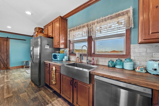 kitchen with sink, ornamental molding, a barn door, and appliances with stainless steel finishes