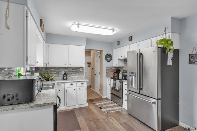 kitchen with white cabinetry, appliances with stainless steel finishes, tasteful backsplash, and light wood-type flooring