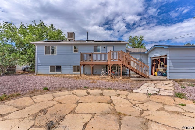 rear view of house with a wooden deck, a patio, and solar panels