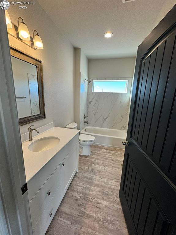 full bathroom with hardwood / wood-style floors, vanity, a textured ceiling, tiled shower / bath, and toilet