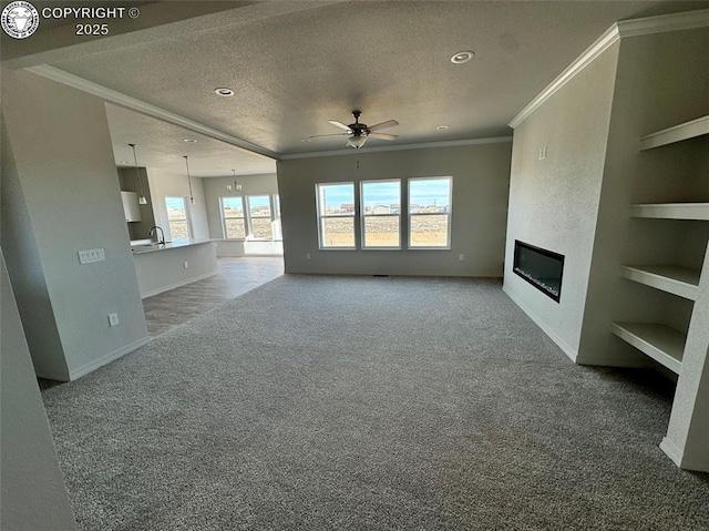 unfurnished living room with built in shelves, a textured ceiling, ornamental molding, carpet floors, and ceiling fan