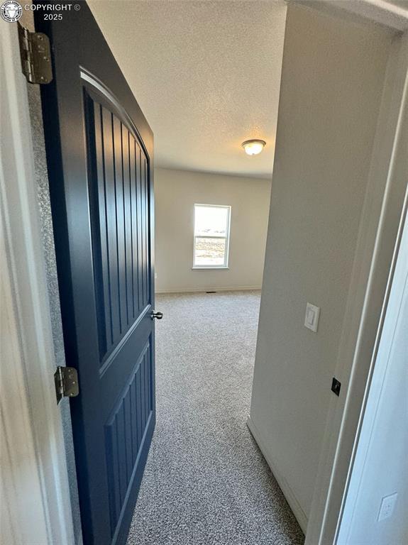 corridor with light carpet and a textured ceiling