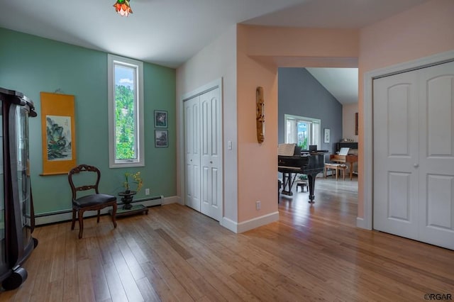 living area featuring a baseboard heating unit, vaulted ceiling, and light wood-type flooring